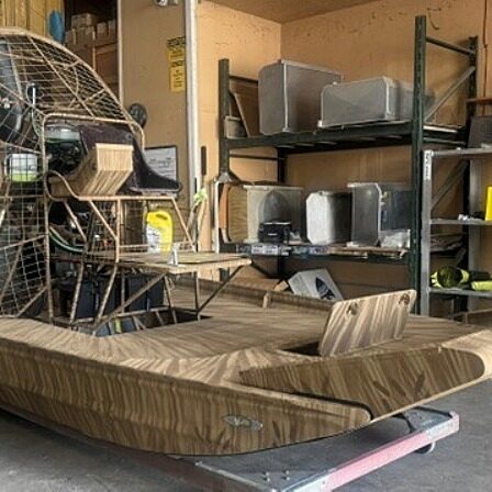Airboat with a circular rear propeller cage, stored in a workshop with metal shelving and tool equipment nearby.